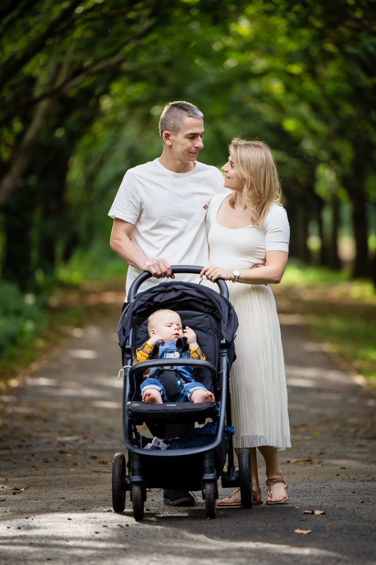 Parents walking with their baby in a pram along a tree-lined path