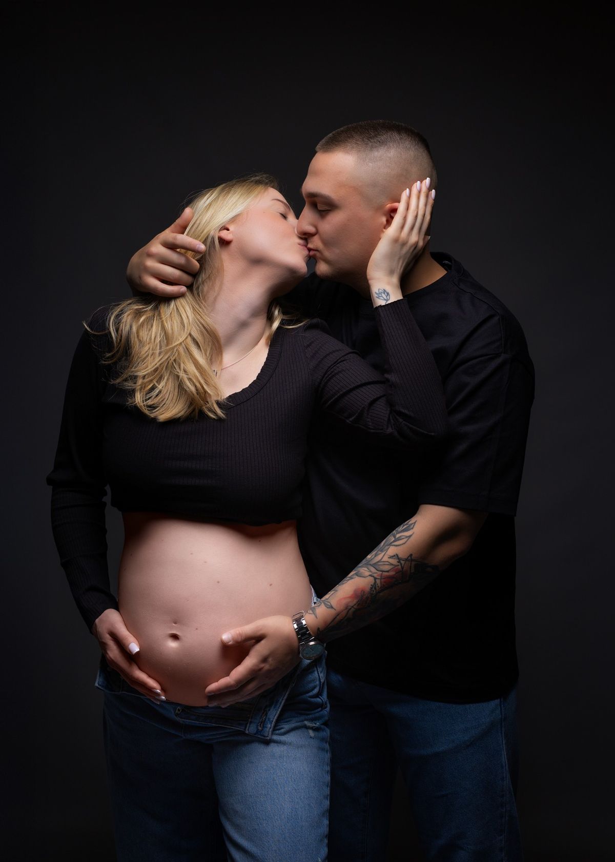 Couple kissing, his hands around her bump, against a dark backdrop