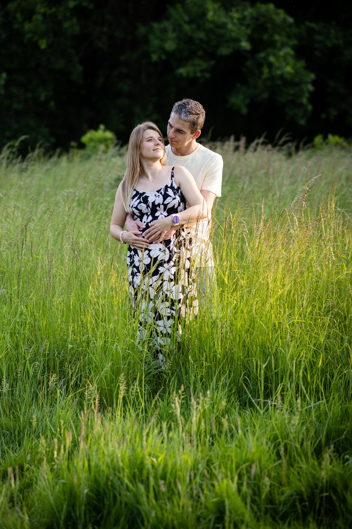 Expectant couple standing together in long summer grass