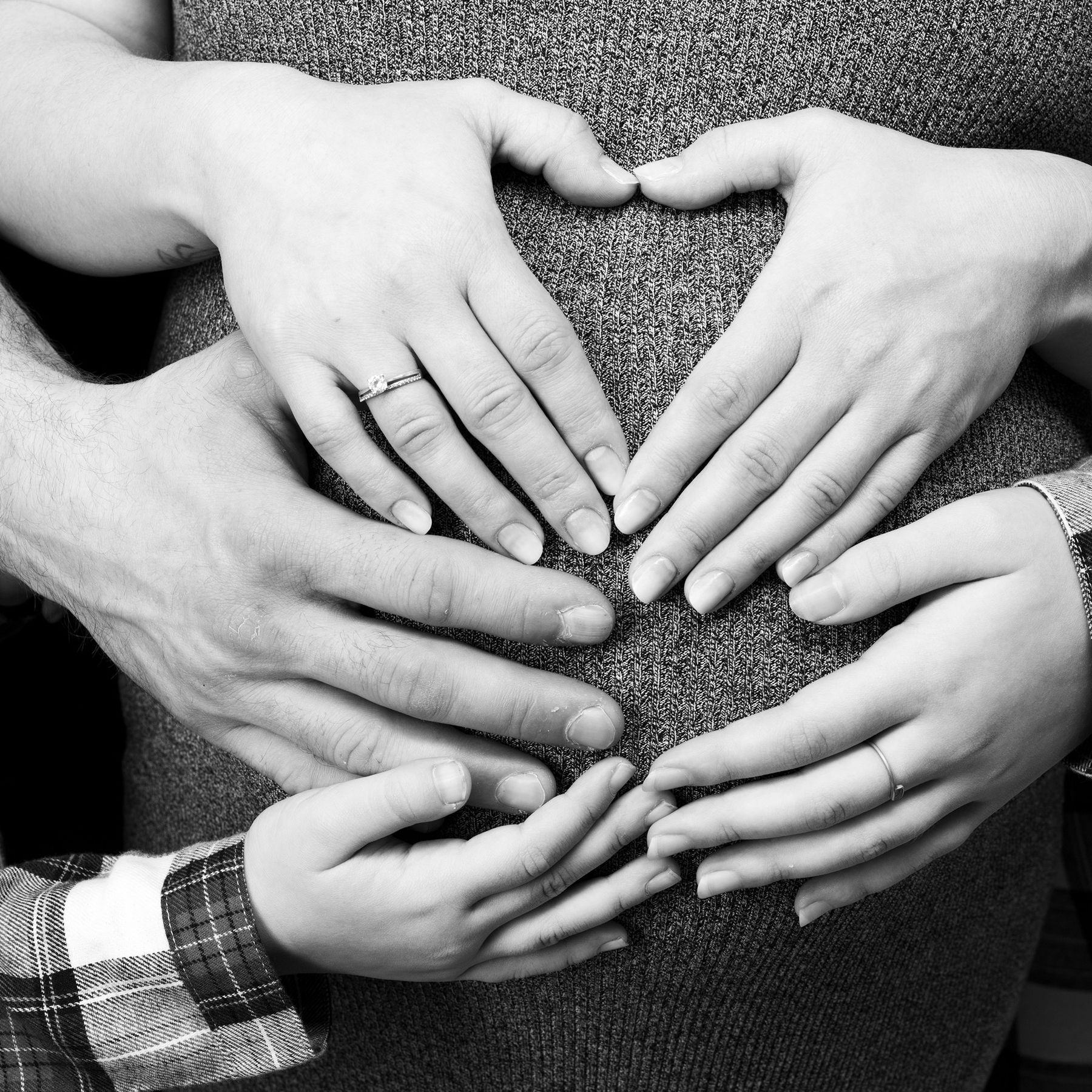 Black and white photo of family hands making a heart on the bump