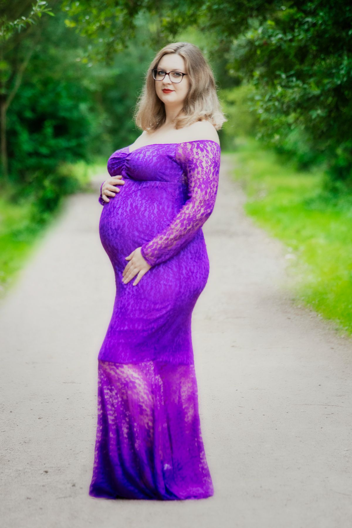 Mum-to-be in a purple lace gown on a woodland path