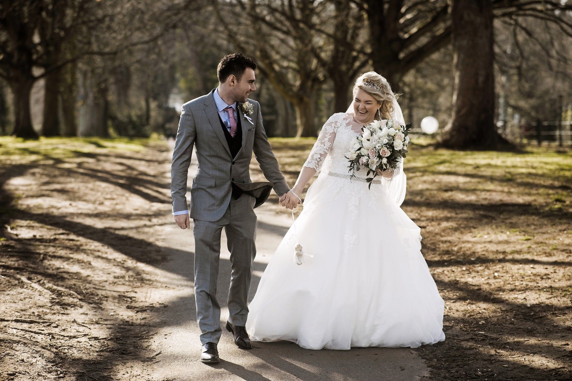 Bride and groom walking hand in hand down an avenue of trees